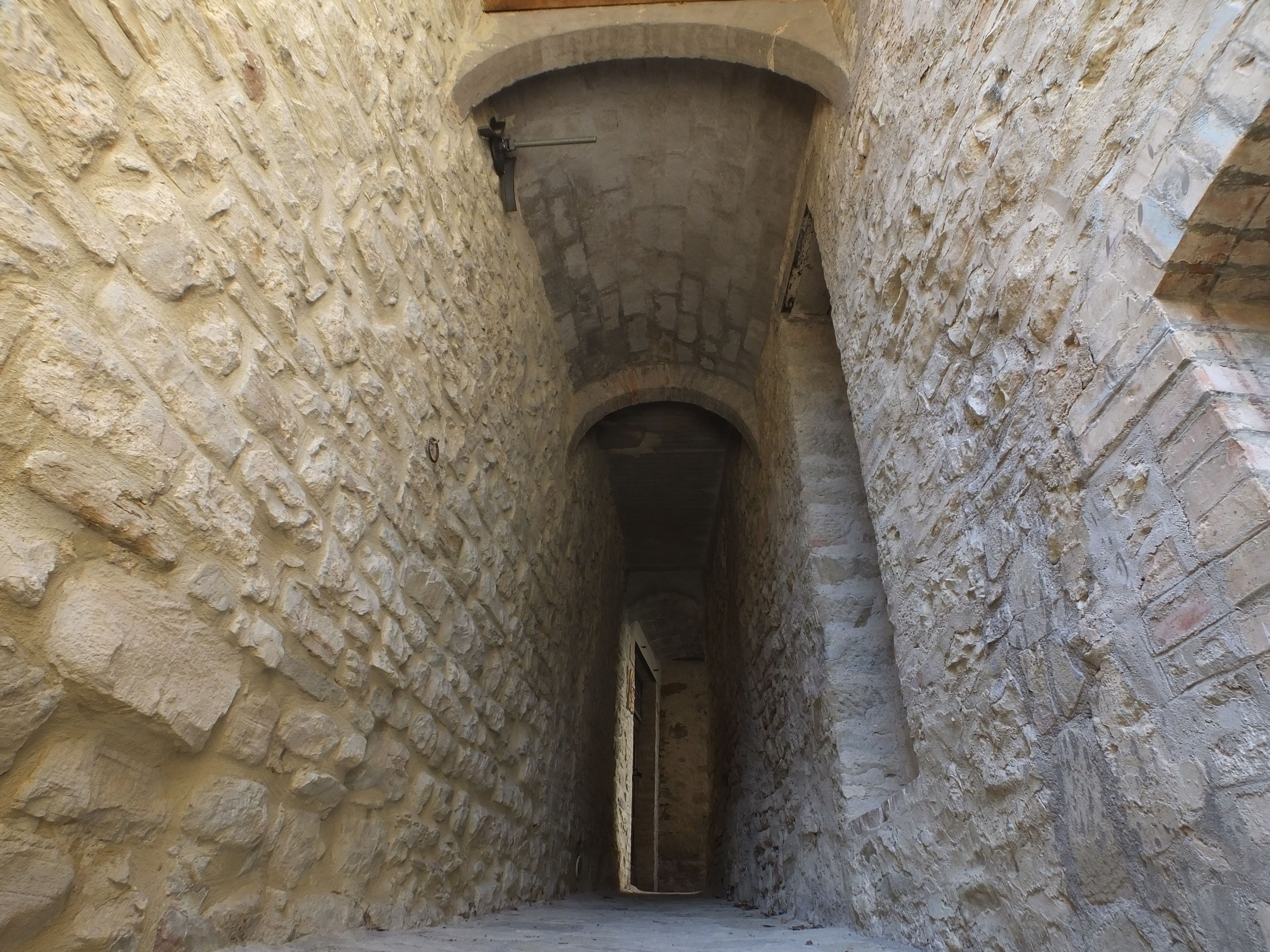 Un étroit couloir en pierre, doté d’un plafond en arc de cercle et d’une porte au fond.