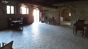 A spacious hall with stone walls, wooden beams, and a herringbone-patterned floor. There are tables and chairs arranged for dining or gatherings. - Castello di Giomici (Valfabbrica)