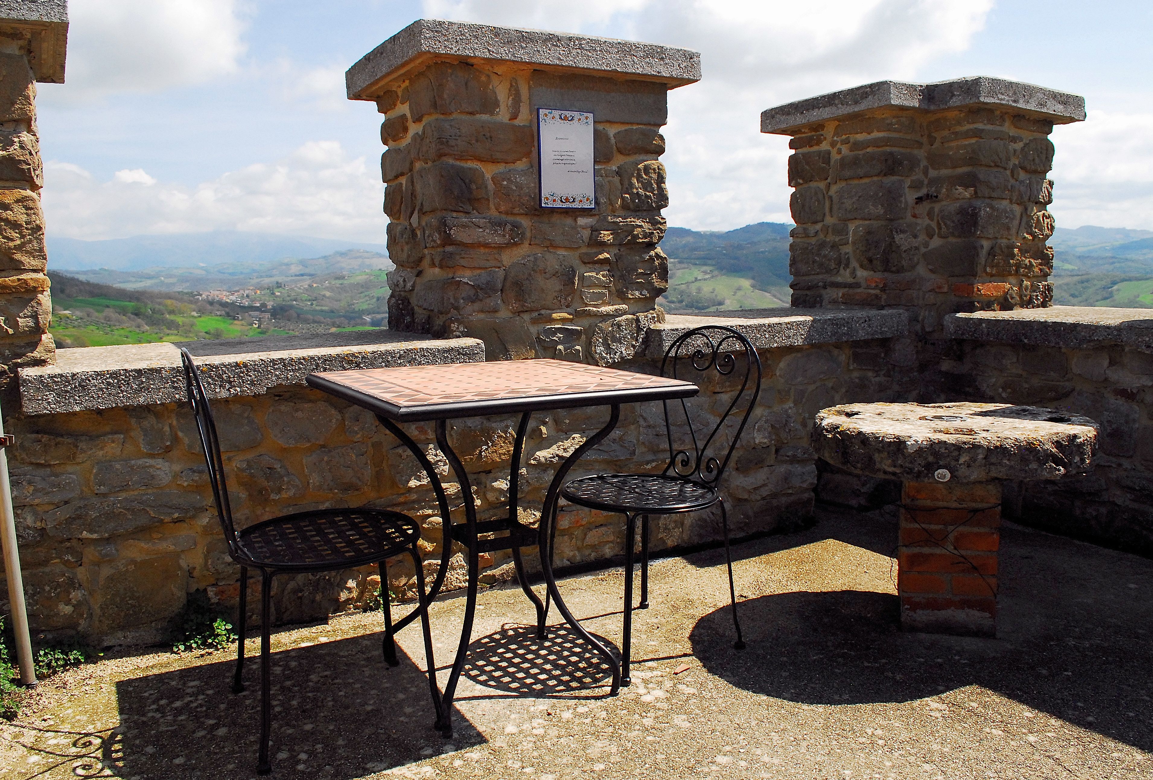 A stone table with chairs, a stone bench, and a view of the countryside.