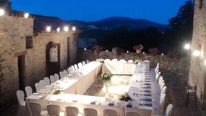 An outdoor dining area with a long table set for a meal, surrounded by stone walls and a mountainous backdrop. - Castello di Giomici (Valfabbrica)
