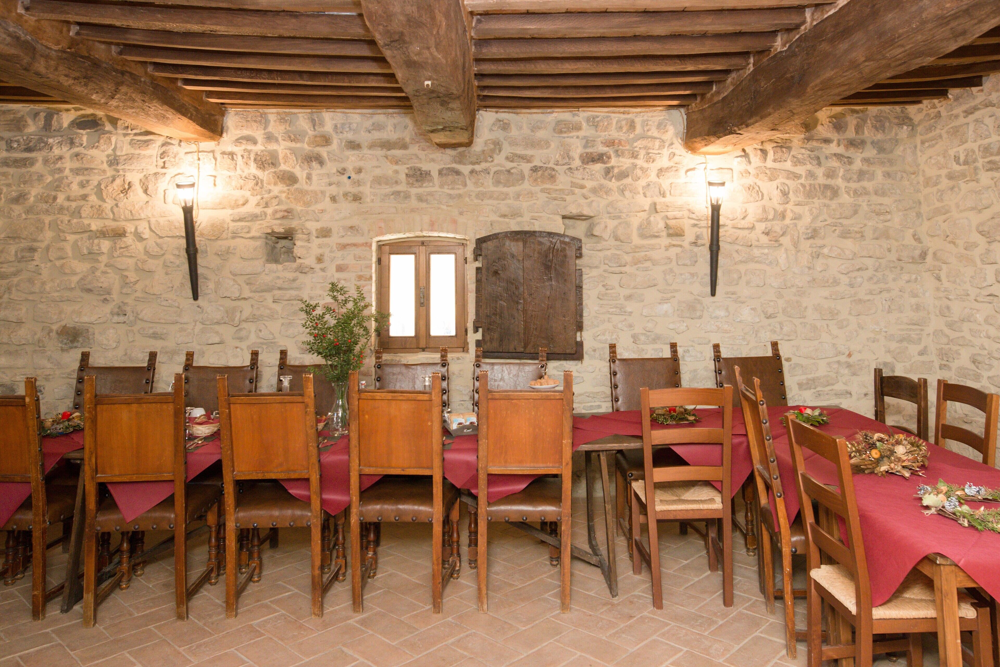 A dining area with wooden tables and chairs, stone walls, and exposed wooden beams.