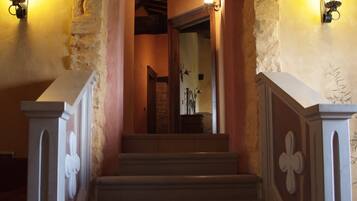 Una escalera con paredes de piedra y techo de madera que lleva a una habitación con chimenea.