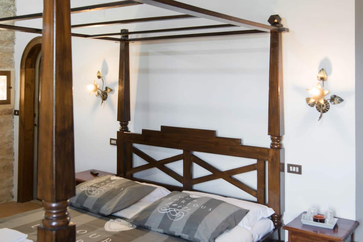 A four-poster bed with a wooden headboard, two wall sconces, and a small wooden nightstand with a tray.