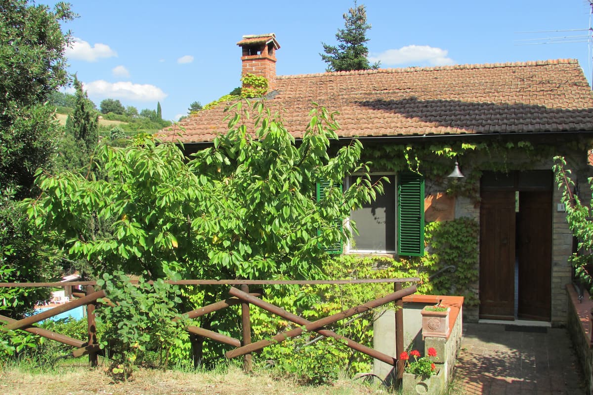 A rustic house with a tiled roof, a chimney, and a wooden gate.