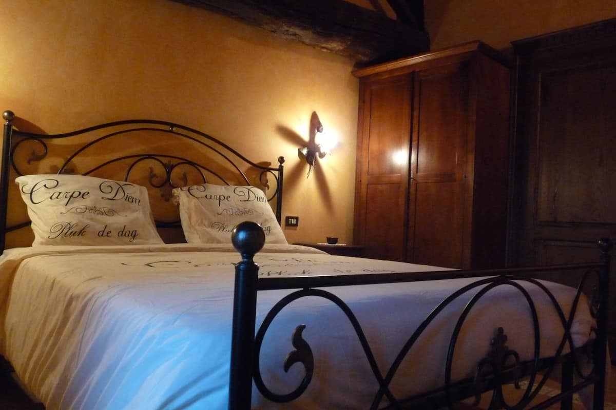 A bed with a metal frame and white bedding, two pillows with text, a wall-mounted light, and wooden furniture in the background.