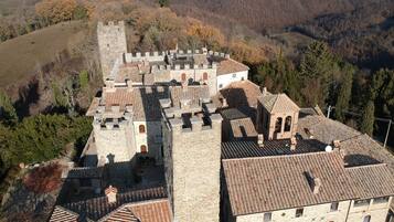 Un bâtiment de style médiéval, avec des murs en pierre et des toits couverts de tuiles, entouré d’arbres et de collines.