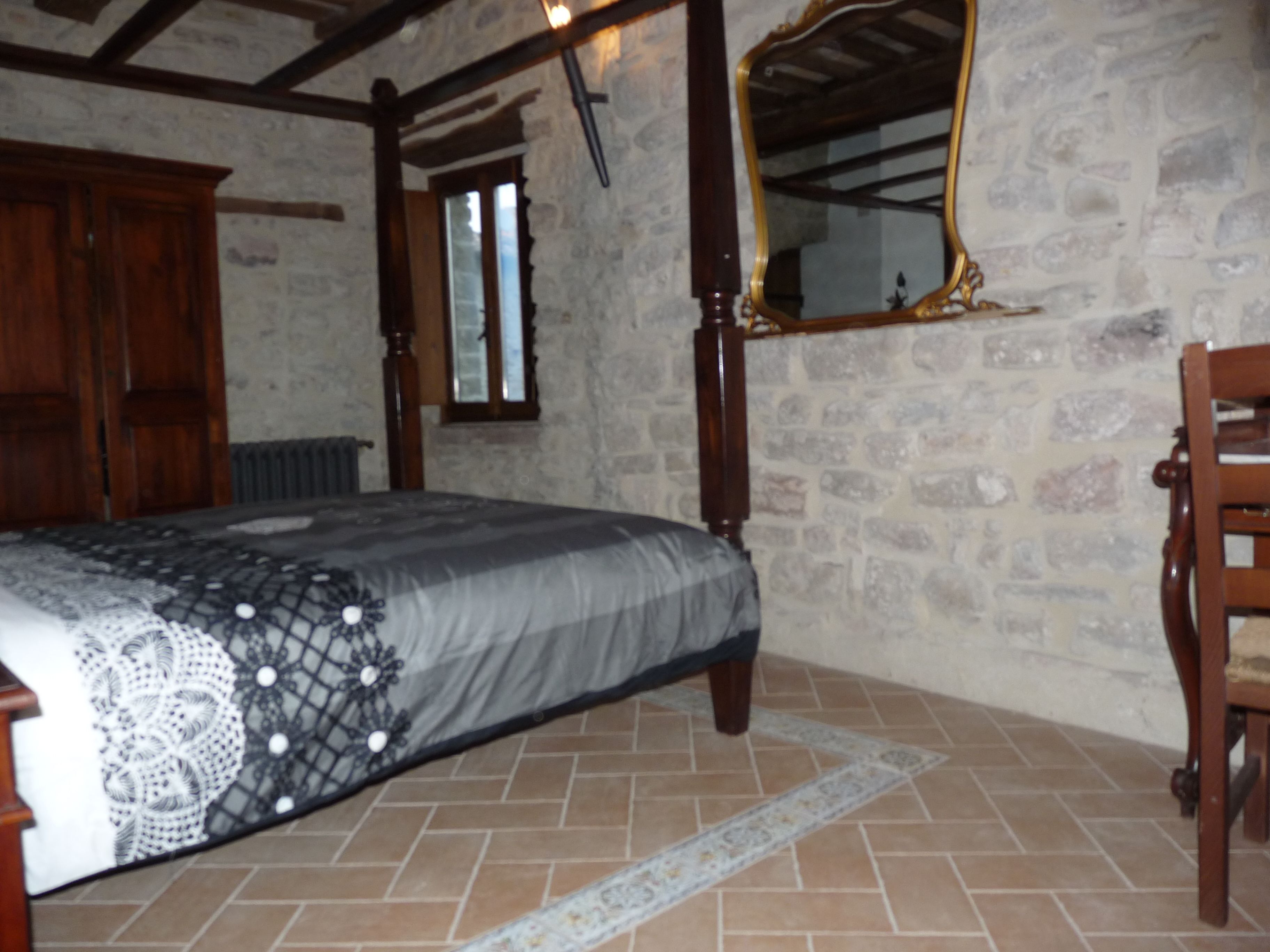 A bedroom with a bed, a wooden wardrobe, a mirror, and a stone wall.