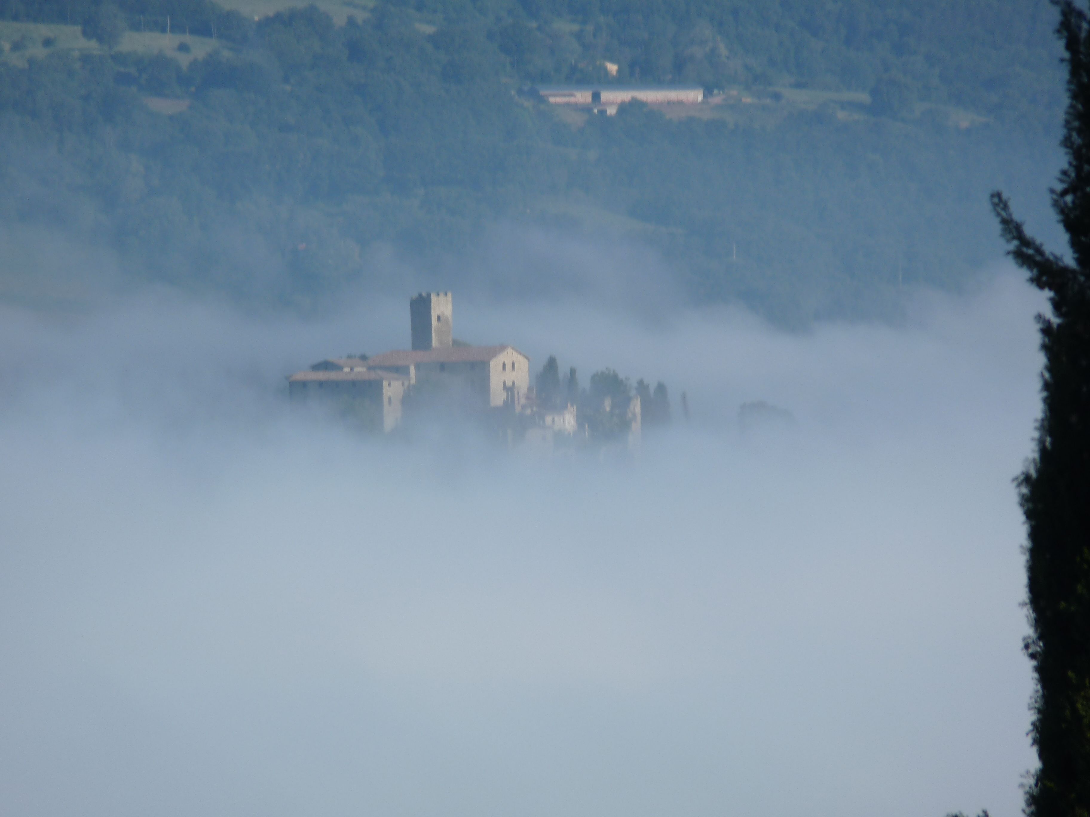 A historic building partially obscured by fog, with a tower and several smaller structures.