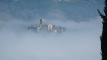 A historic building partially obscured by fog, with a tower and several smaller structures.