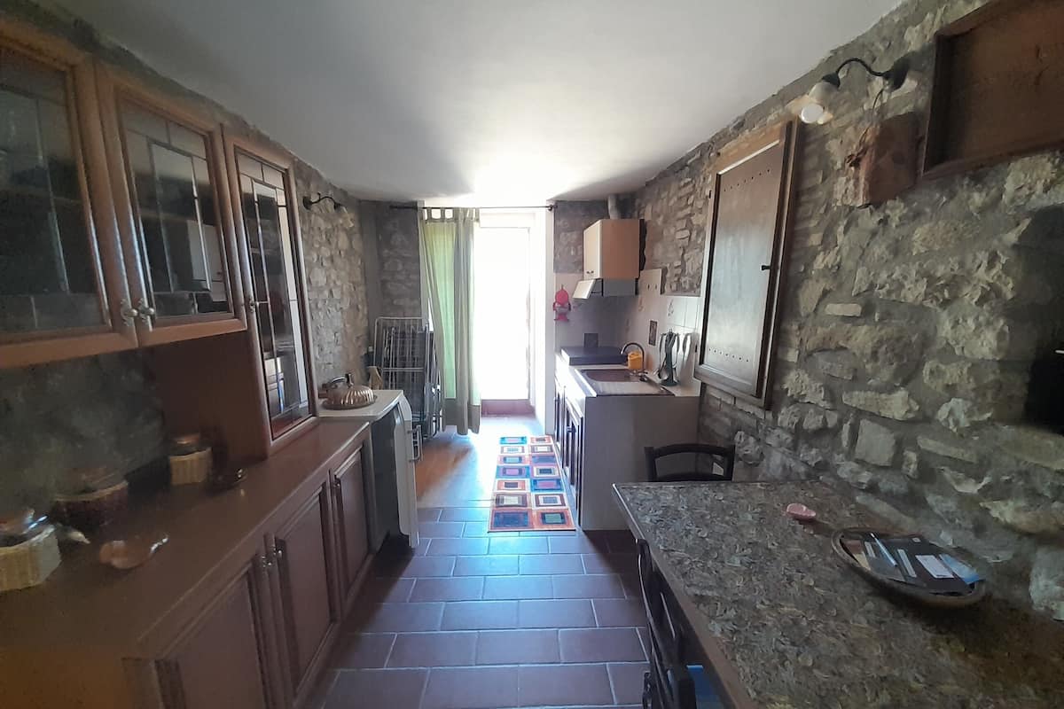 A kitchen with stone walls, wooden cabinets, and a tiled floor.