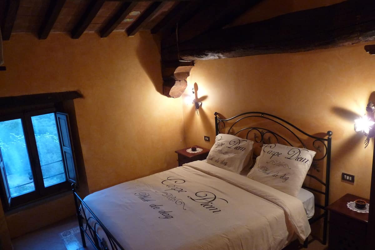 A bedroom with a bed, a nightstand, a wall-mounted lamp, a window, and a wooden ceiling.