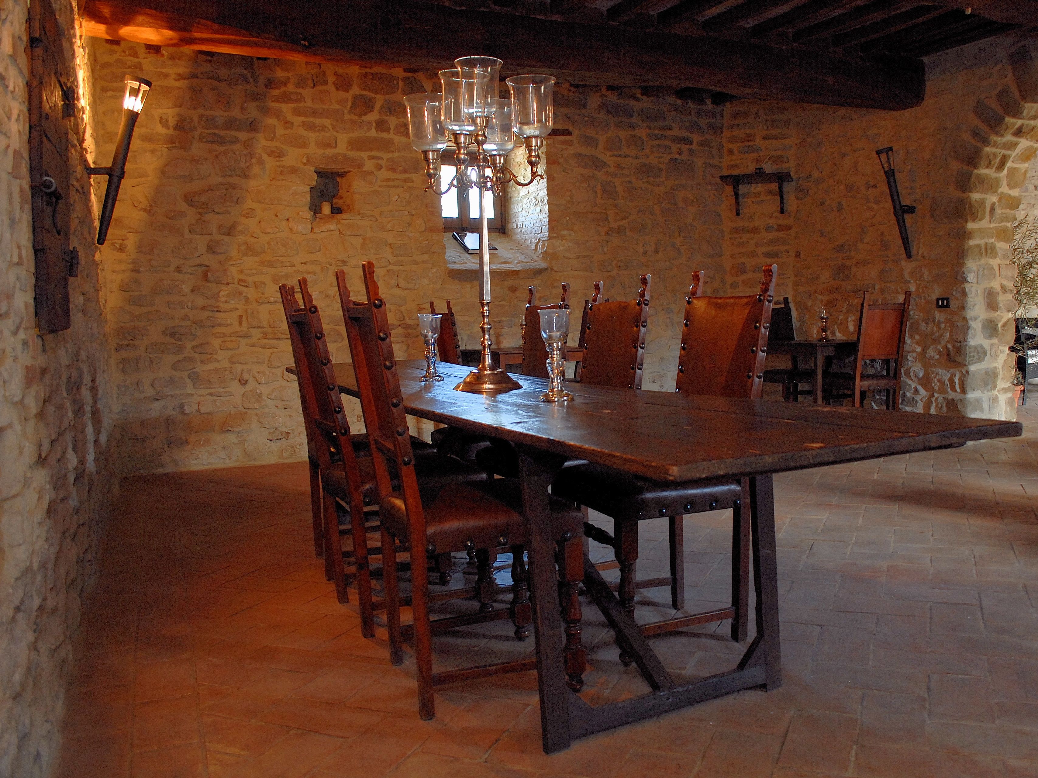 A rustic stone-walled dining area with a wooden table and chairs, a candelabra, and wall-mounted lights.