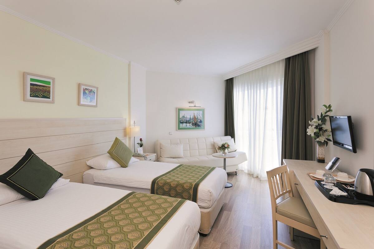 Habitación de hotel con dos camas, un sofá, un escritorio y un televisor.