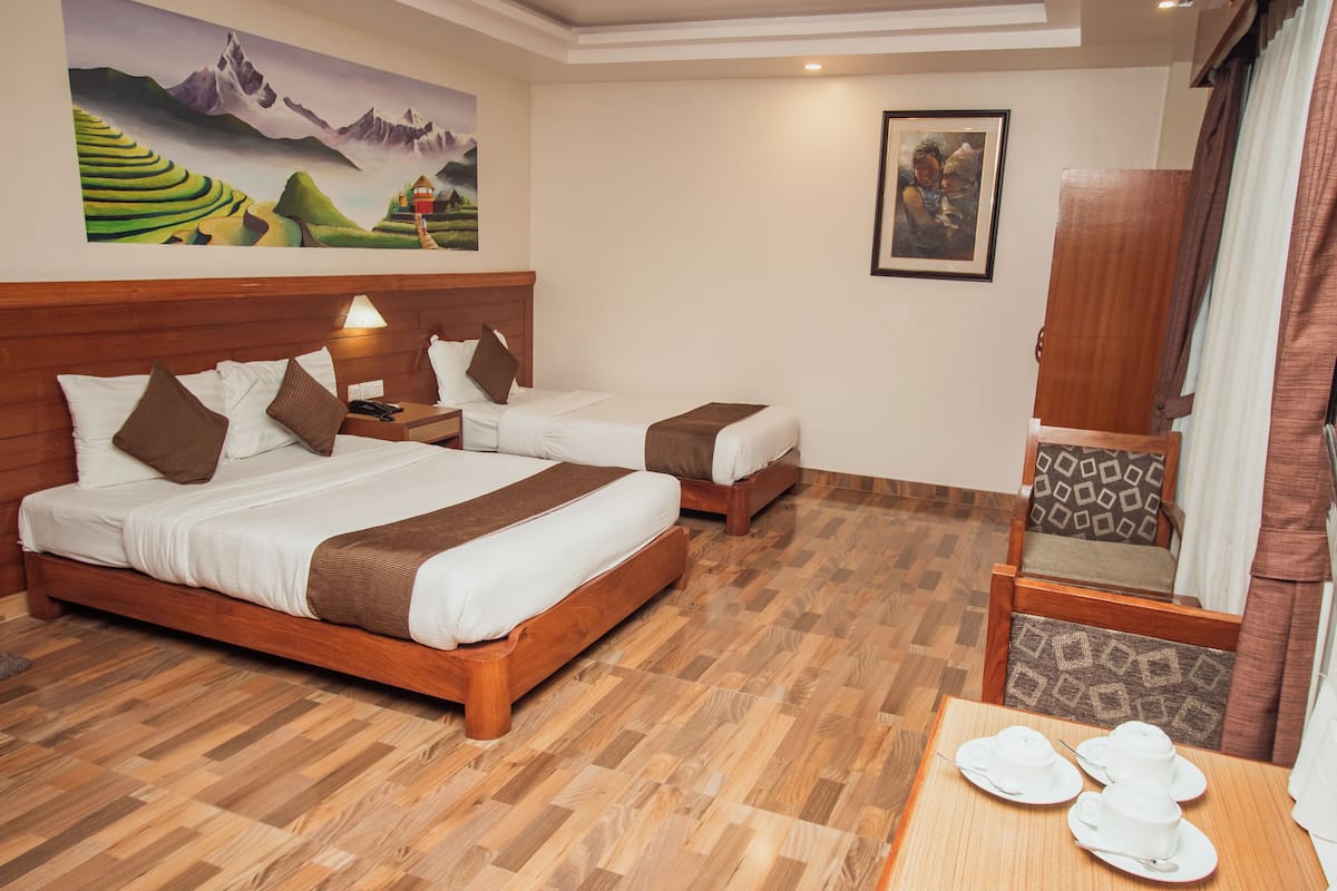 A hotel room with two beds, wooden flooring, a dining table with white tableware, and artwork on the walls.