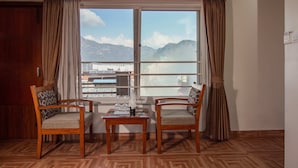 A room with two wooden chairs, a small table, and a large window with curtains. - Mount View Pokhara (Pokhara)