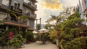 A hotel with a terrace featuring outdoor seating and umbrellas, surrounded by lush greenery and a mountainous backdrop. - Mount View Pokhara (Pokhara)