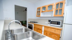Una cocina con armarios de madera, un lavamanos de acero inoxidable, un microondas y un refrigerador.