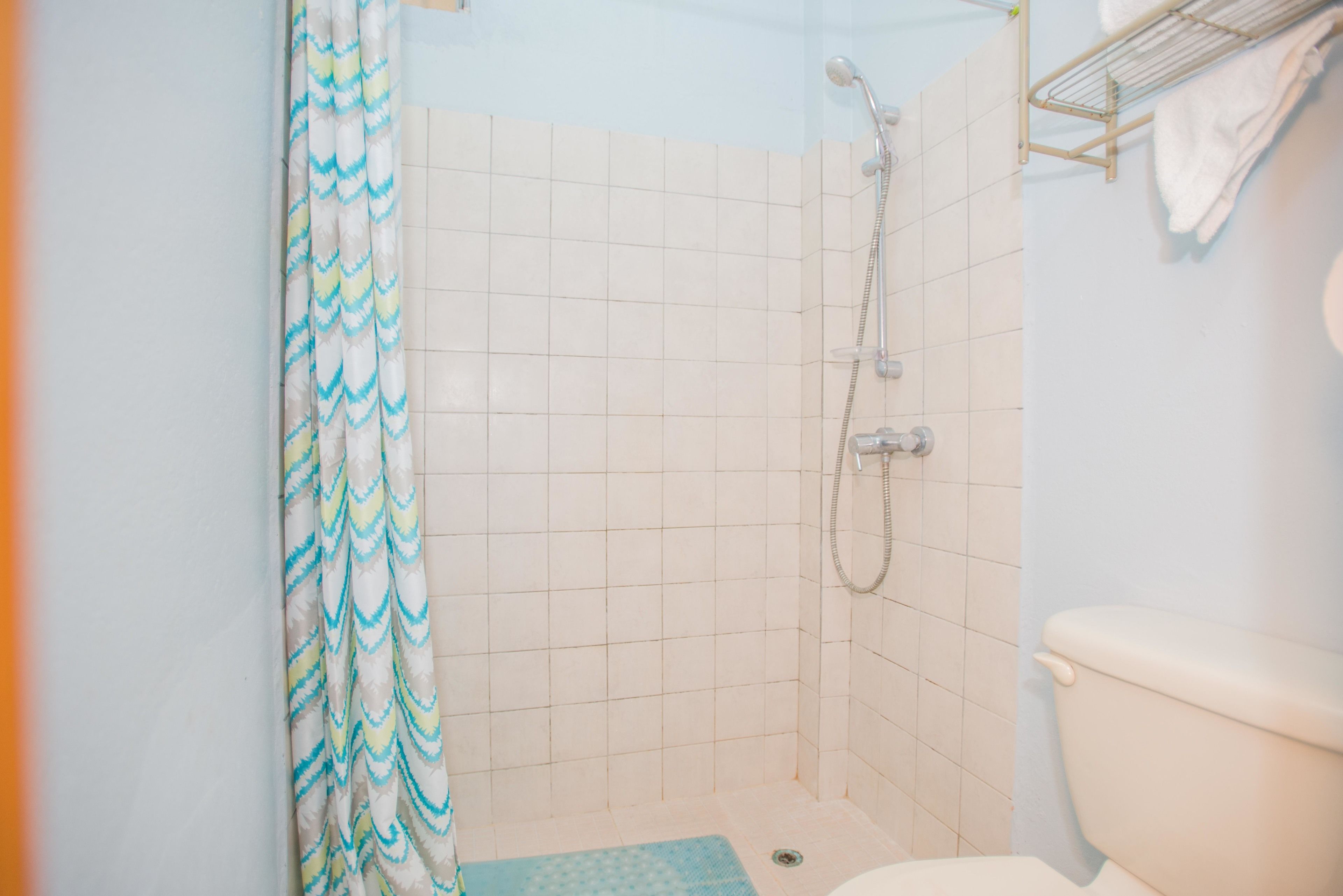 Une petite cabine de douche carrelée, équipée d’un pommeau de douche, de toilettes et d’un porte-serviettes.