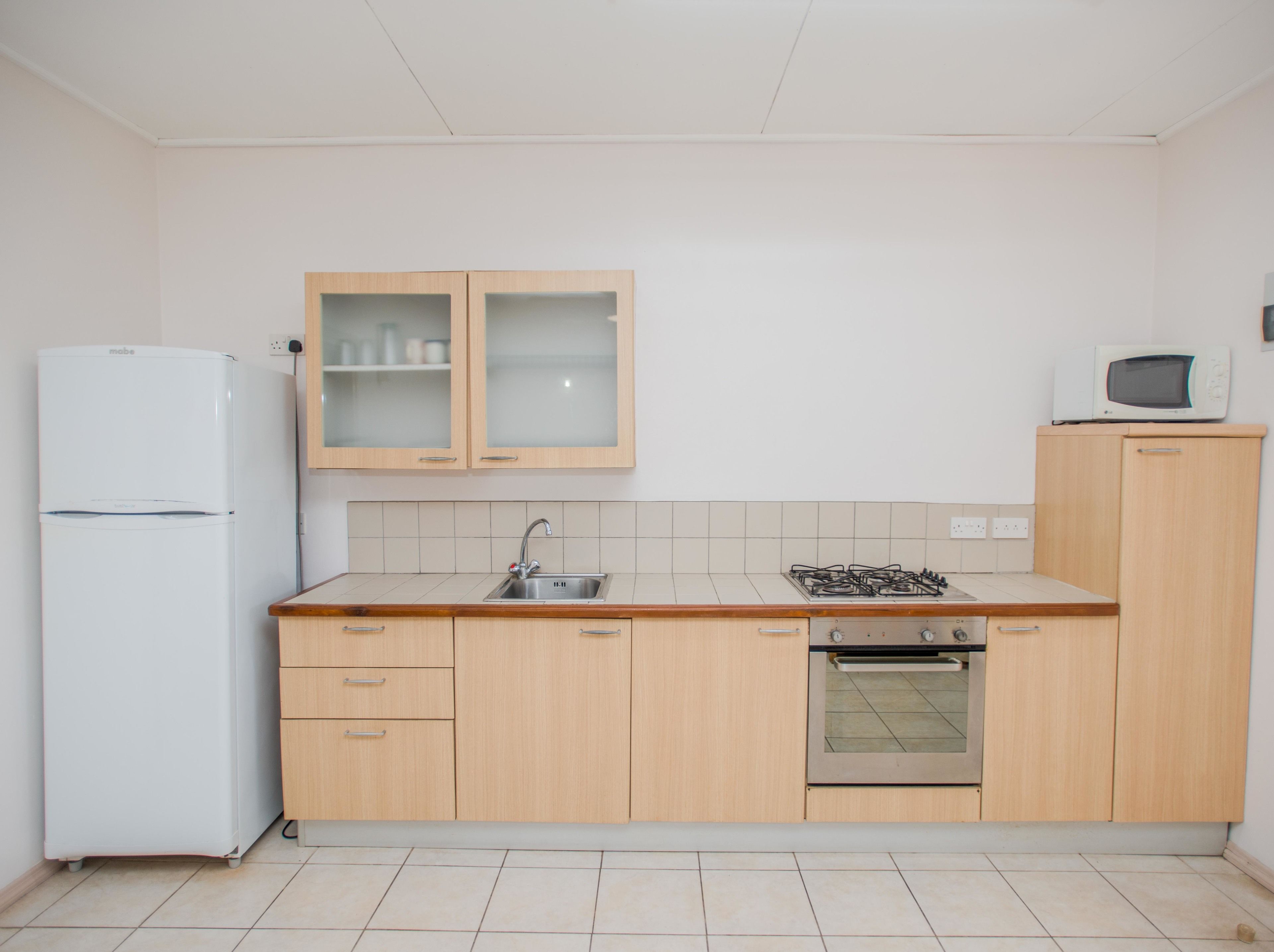 Eine Küche mit Holzausstattung, einem weißen Kühlschrank, einem Herd, einer Mikrowelle und einem Spülbecken.