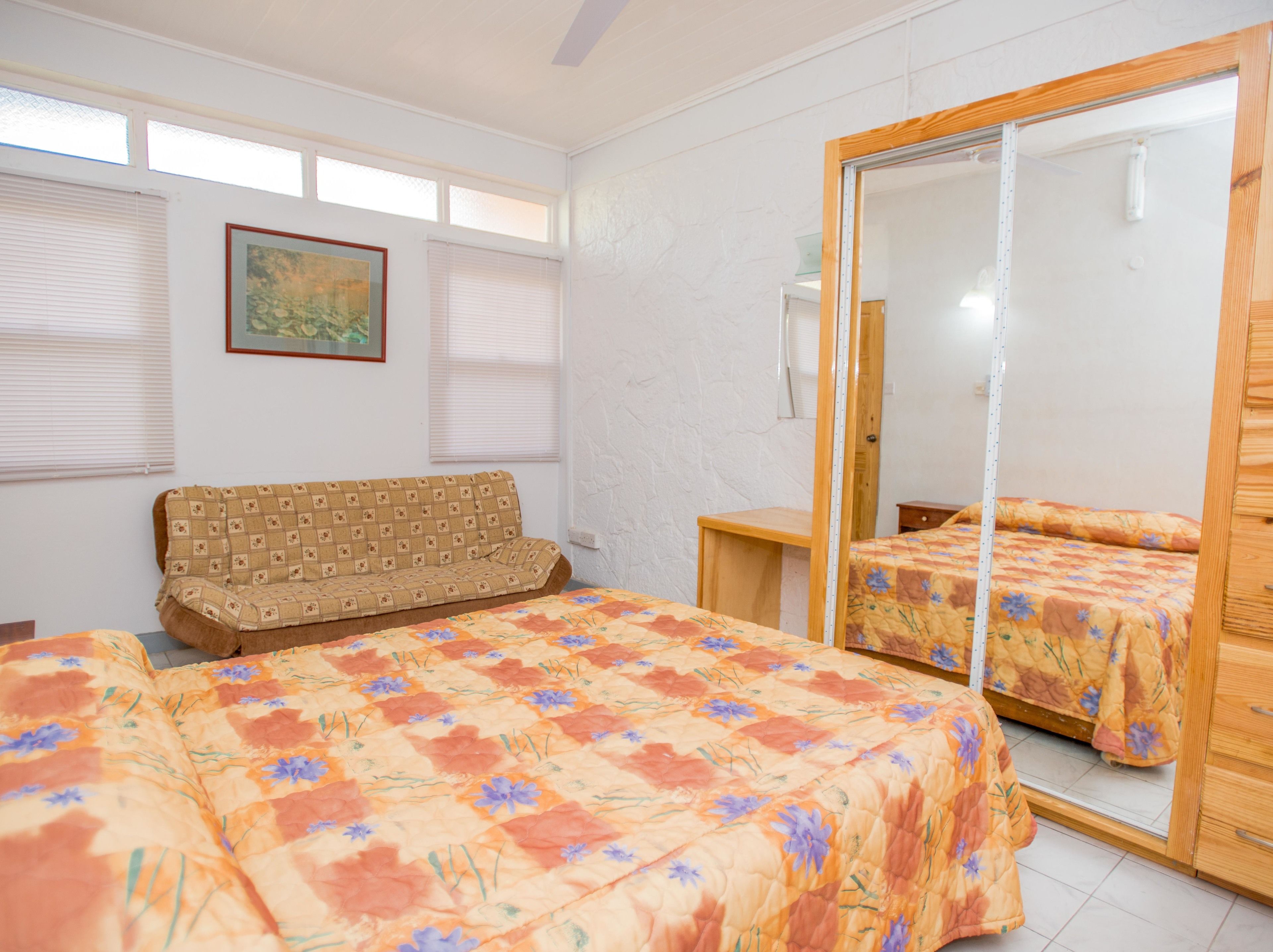 A bedroom with two beds, a sofa, a large mirror, and a window with blinds.