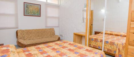 A bedroom with two beds, a sofa, a large mirror, and a window with blinds.