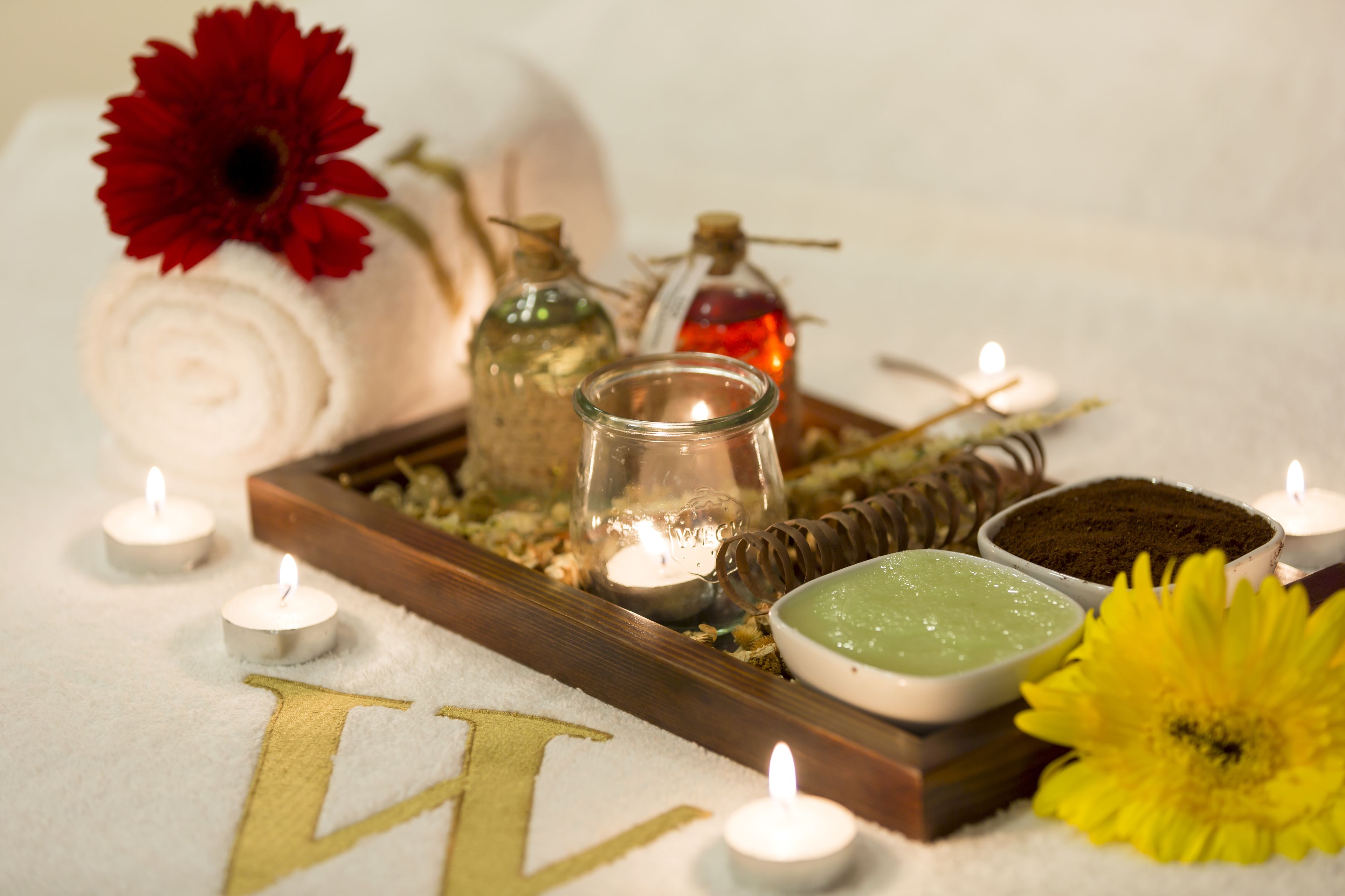A spa setting with candles, a rolled towel, and various bath products.