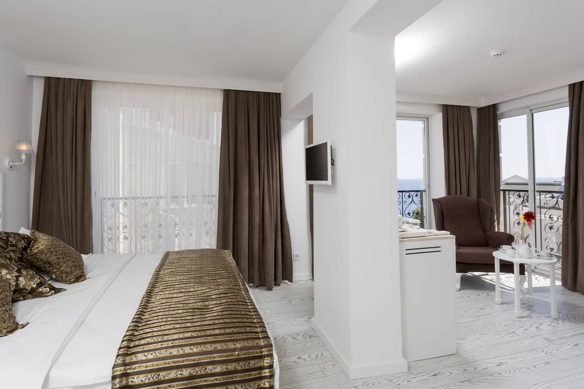 A hotel room with a bed, a desk, a chair, a TV, and a balcony with a view.