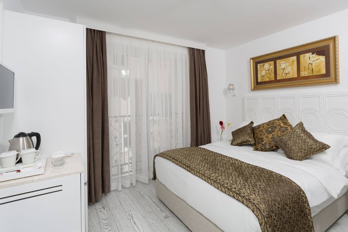 A hotel room with a bed, a bedside table with a lamp, a painting above the bed, and a television on the wall.