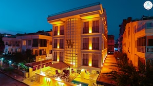 A hotel with a prominent 'W' logo, multiple balconies, and a well-lit outdoor area. - Wise Hotel Spa & Adult Only (Antalya)