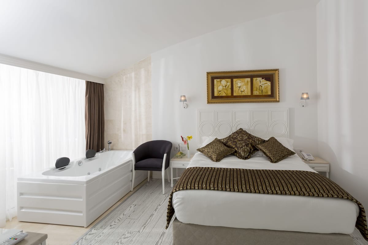 A hotel room with a large bed, a sitting area with a chair, a desk, and a bathtub.