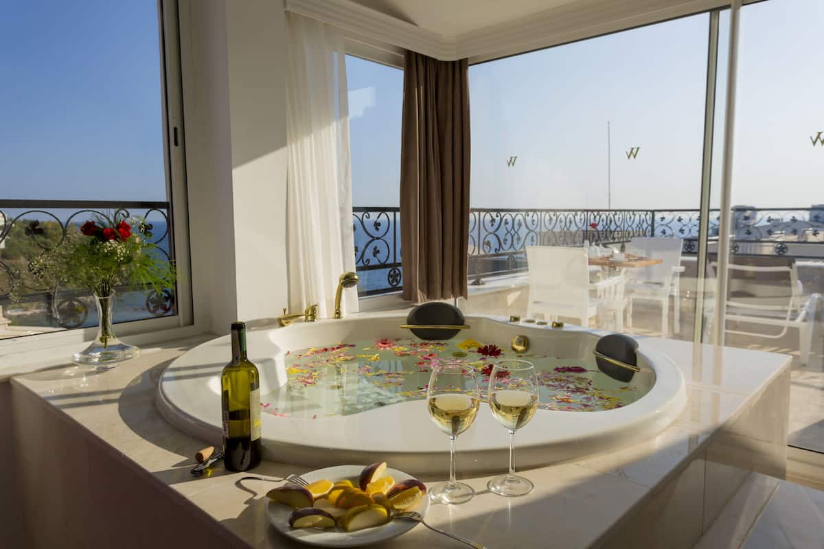 A luxurious bathroom with a bathtub, a wine bottle, and glasses of wine on a counter.