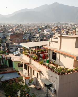 A hotel with a rooftop garden, a sign for 'Nirvana Peace Home', and a view of a densely populated cityscape with mountains in the background. - Kathmandu Sunny Hotel (Kathmandu)