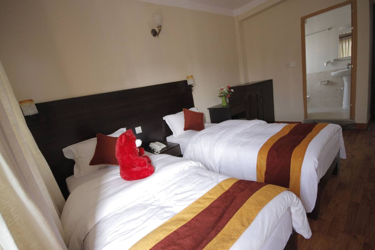 A hotel room with two beds, a nightstand, a mirror, and a bathroom visible through an open door.