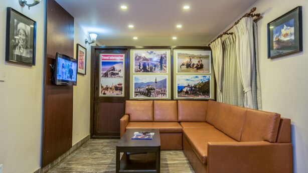 A cozy lobby with a leather sofa, a small table, and a TV screen displaying travel information. - Kathmandu Sunny Hotel (Kathmandu)