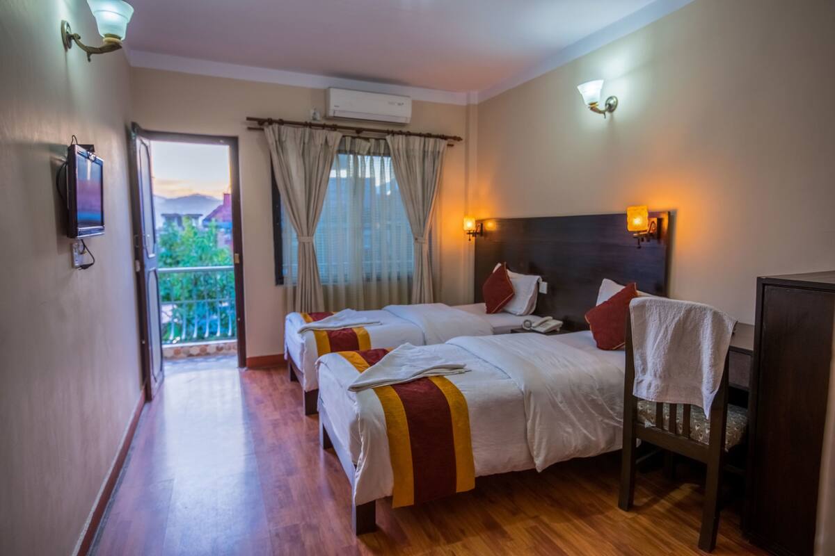 A hotel room with two beds, a TV, a balcony with curtains, and a view of the outdoors.