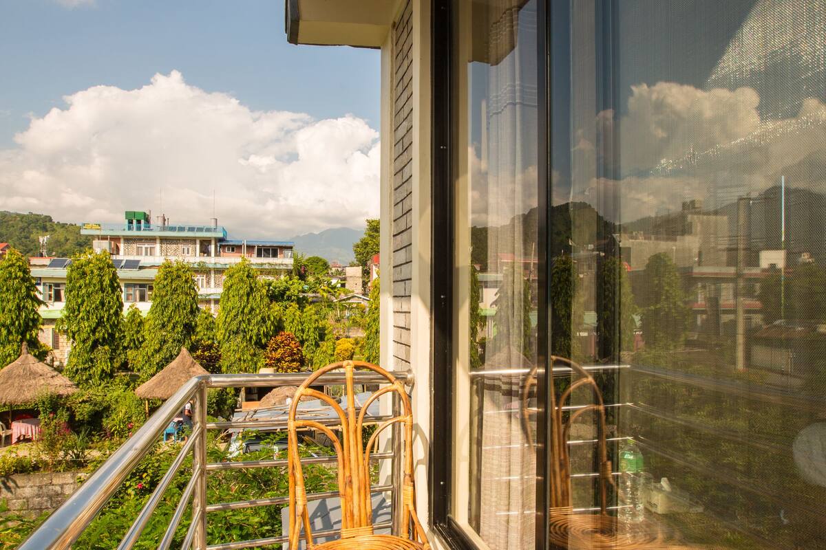 Un balcón con mobiliario de mimbre, una puerta de vidrio y vistas a edificios y árboles.