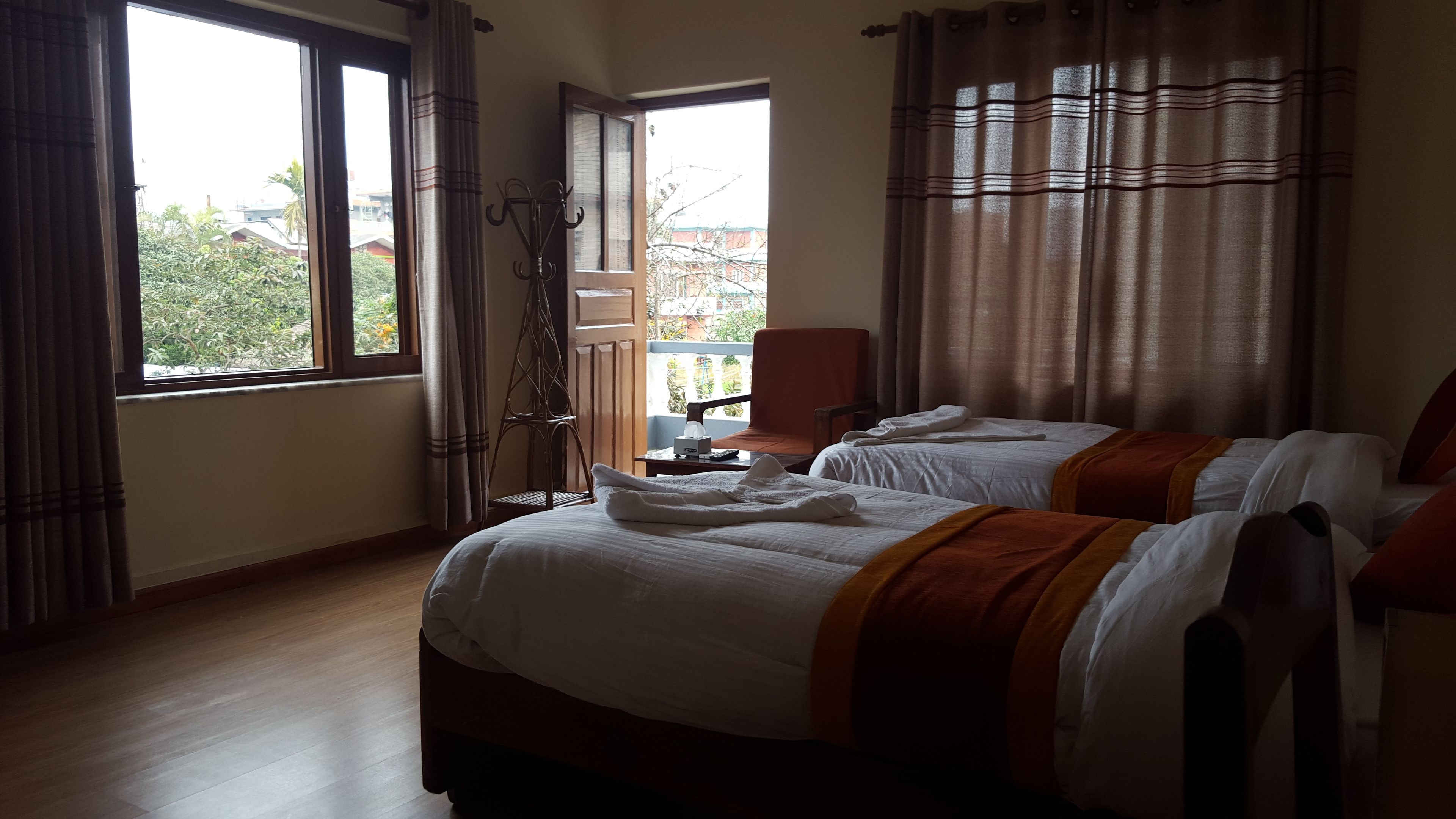 Une chambre d’hôtel avec deux lits, une fenêtre avec des rideaux, une chaise et une petite table sur laquelle se trouve une boîte de mouchoirs.