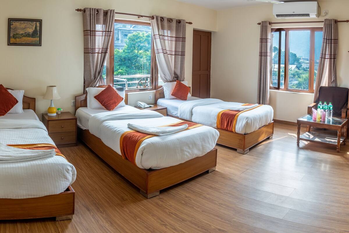 Habitación de hotel con dos camas individuales, suelo de madera, ventana con cortinas, armario de madera y una mesita con botellas.