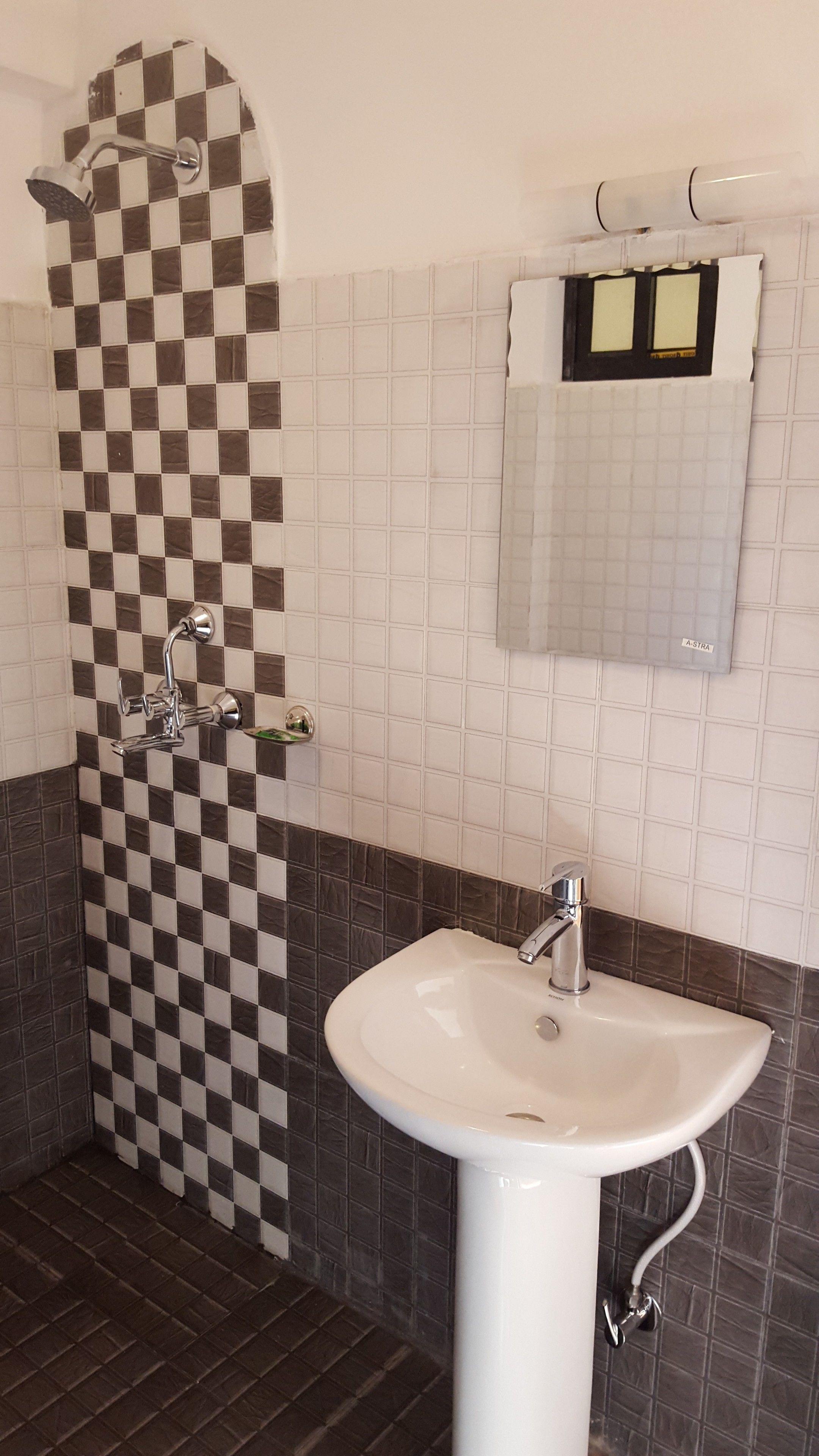 A bathroom with a checkered shower wall, a white sink, and a mirror with a towel hanging on the wall.