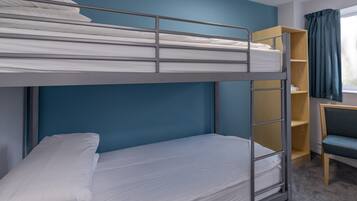 Una cama literera con ropa de cama blanca, un escritorio con silla y una estantería.