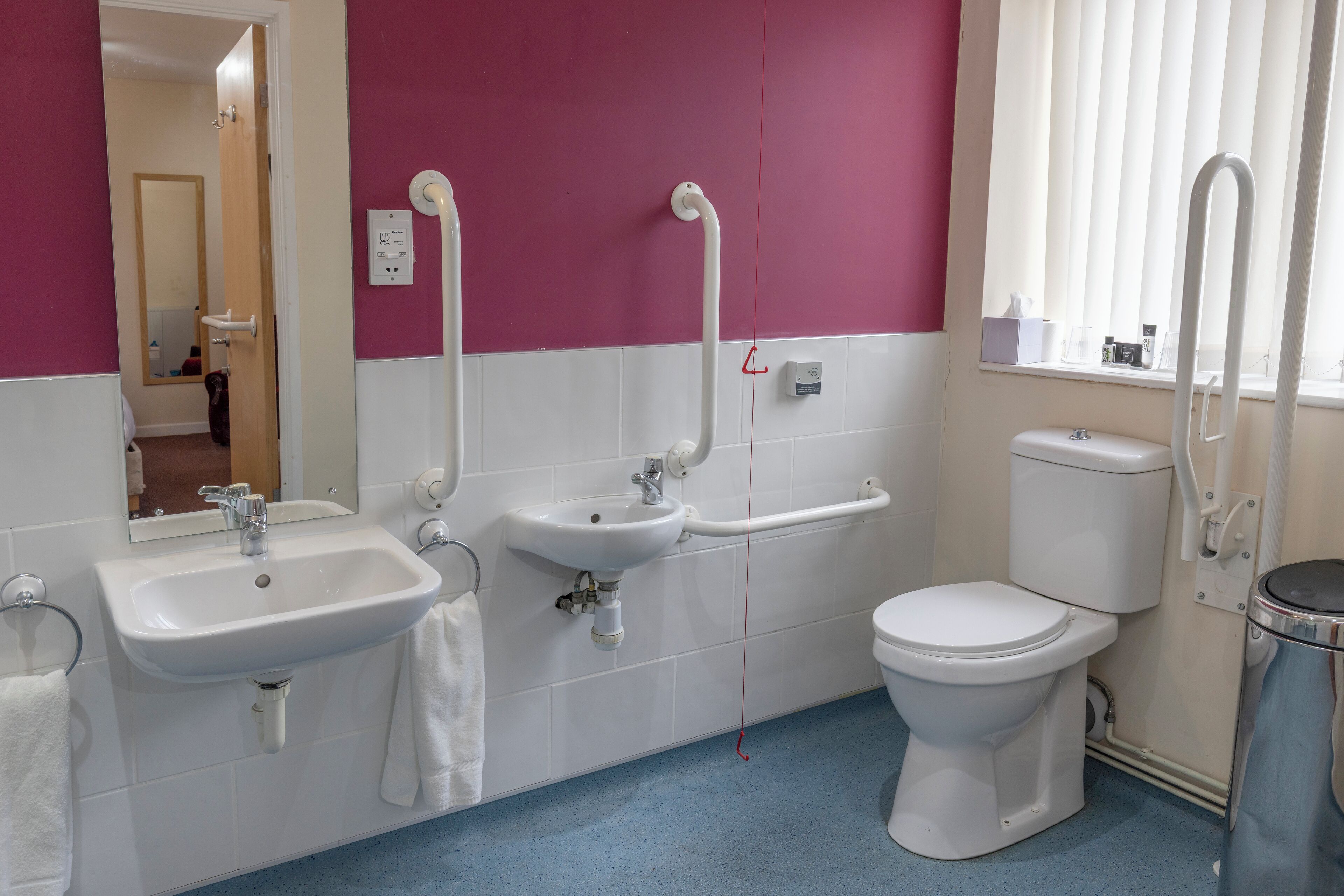 A bathroom with a sink, mirror, toilet, and window with blinds.