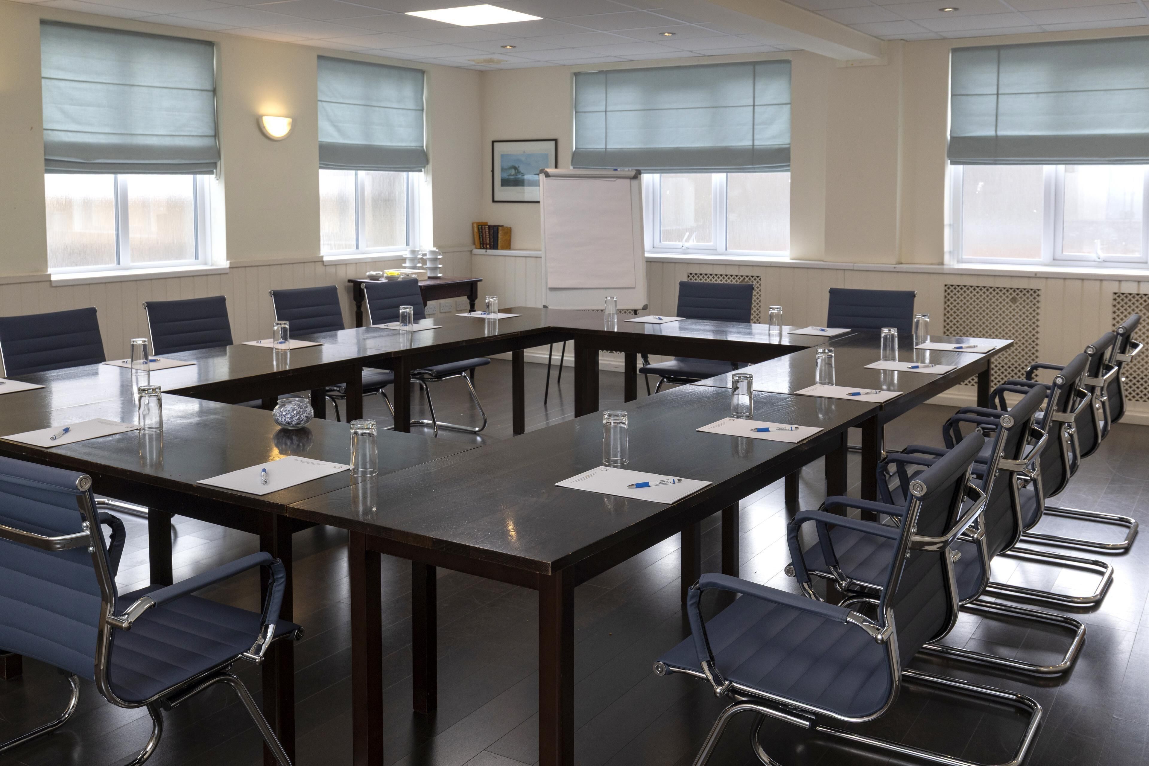 A conference room with a long table, chairs, a whiteboard, and windows with blinds.