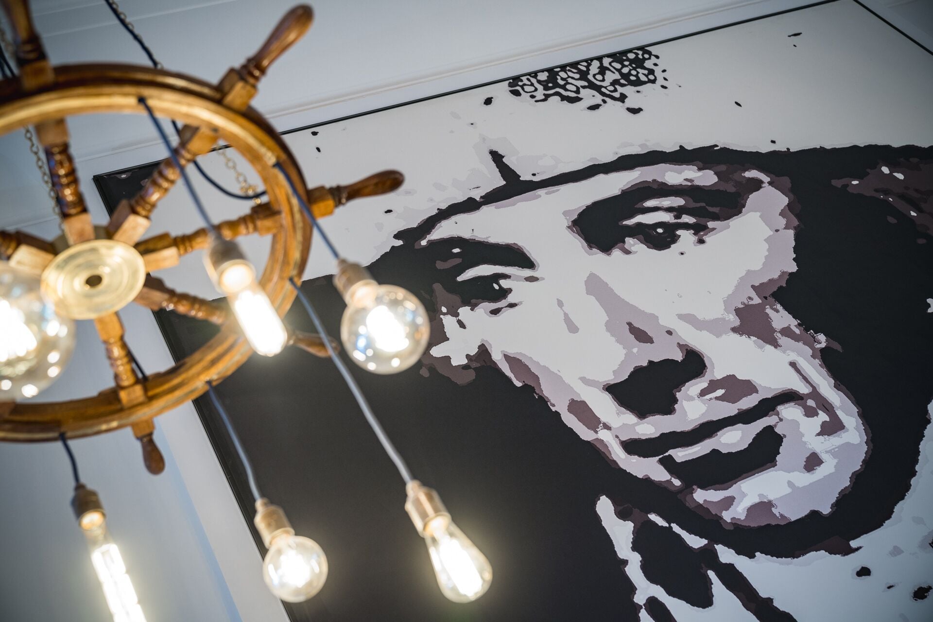 Un mur orné d’un grand portrait stylisé et un plafond décoré d’un gouvernail de navire et de luminaires suspendus.
