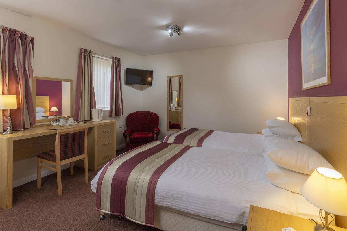 A hotel room with a bed, desk, chair, TV, and a mirror.