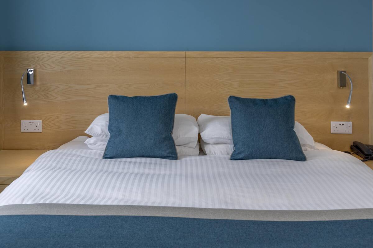 A bed with a wooden headboard, two pillows, and a bedside table with a lamp.
