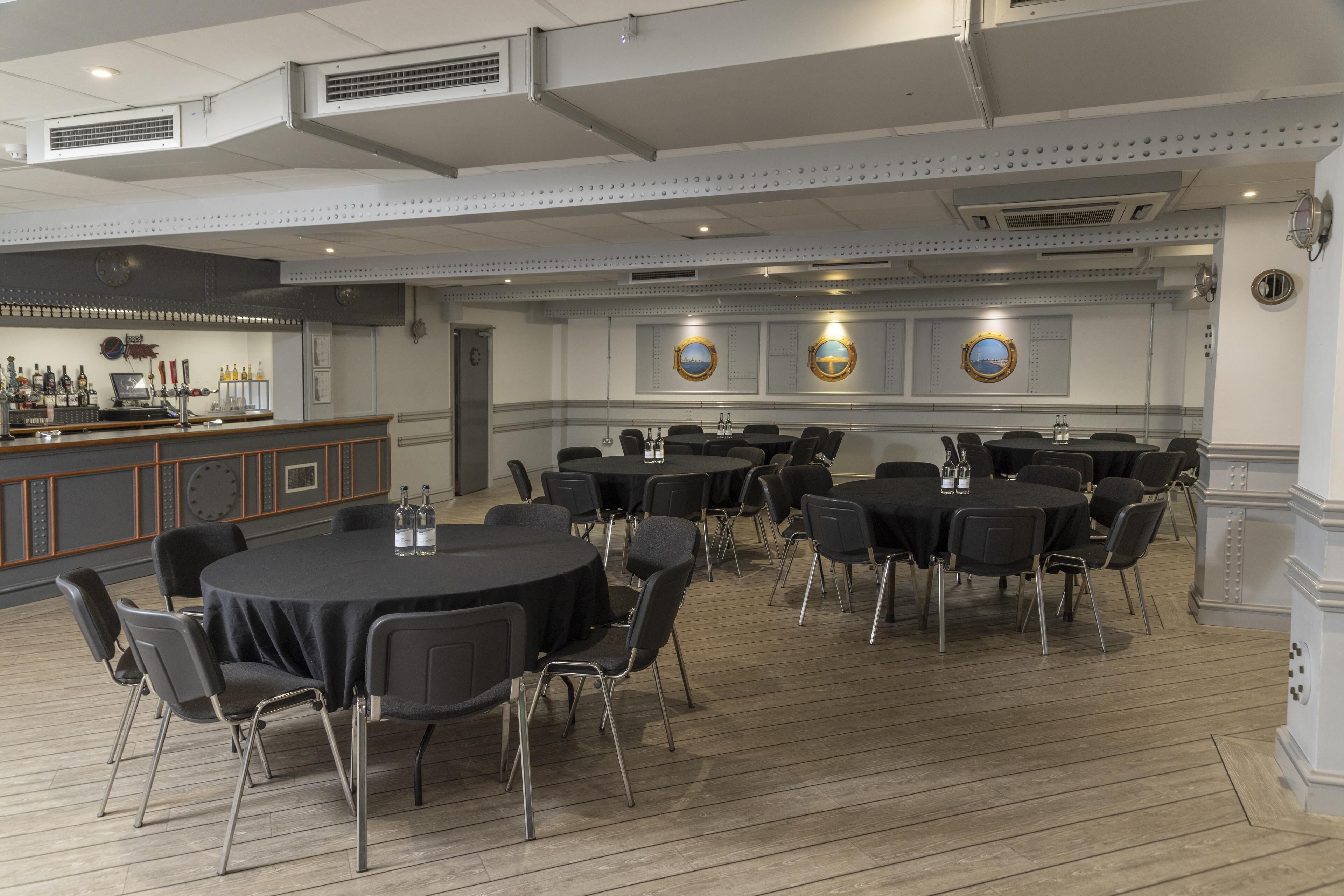 A conference room with round tables, black chairs, and a bar area with bottles.