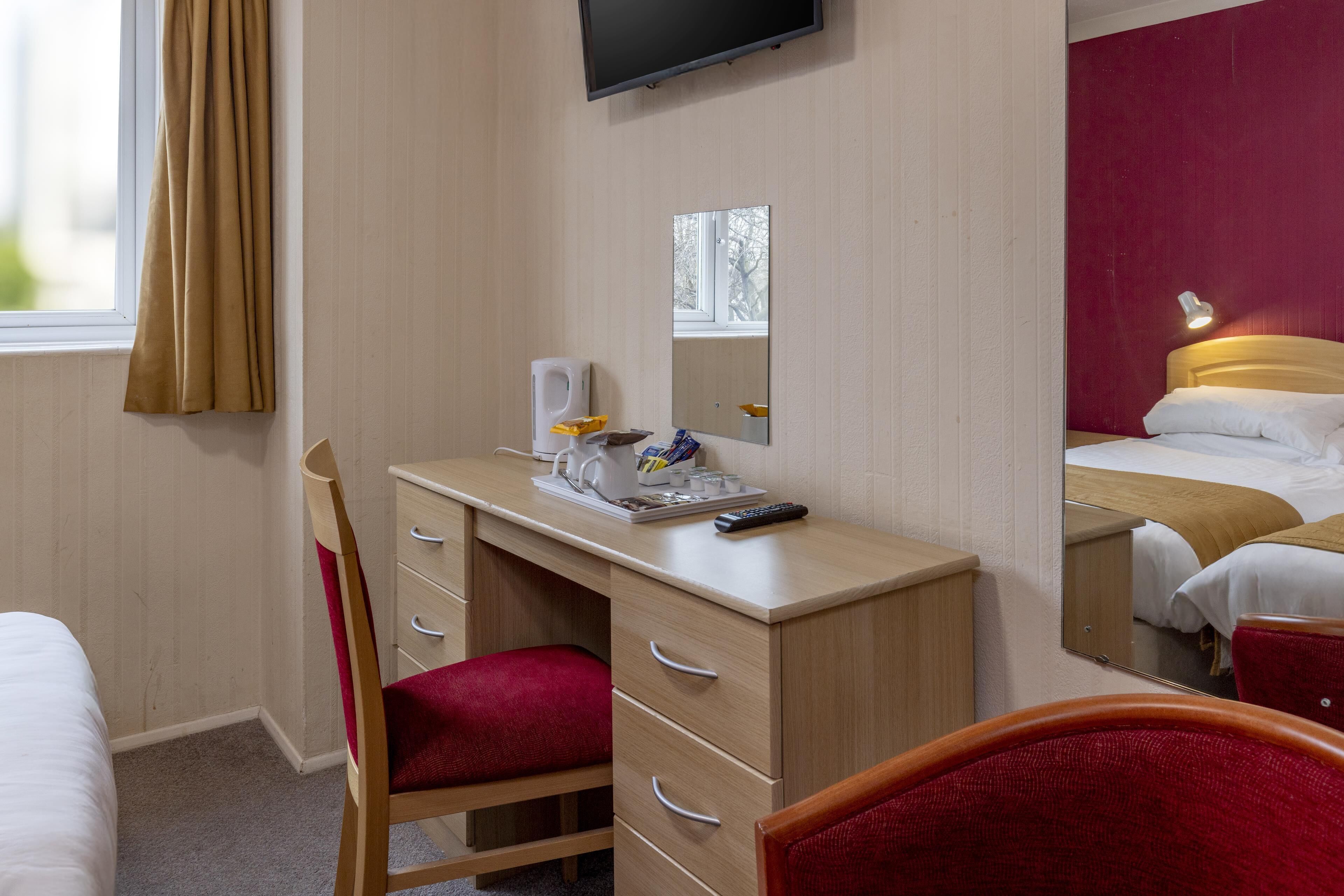 A hotel room with a desk, chair, and a bed with a red headboard.