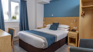 A hotel room with a bed, bedside table, chair, wardrobe, and a window with curtains.