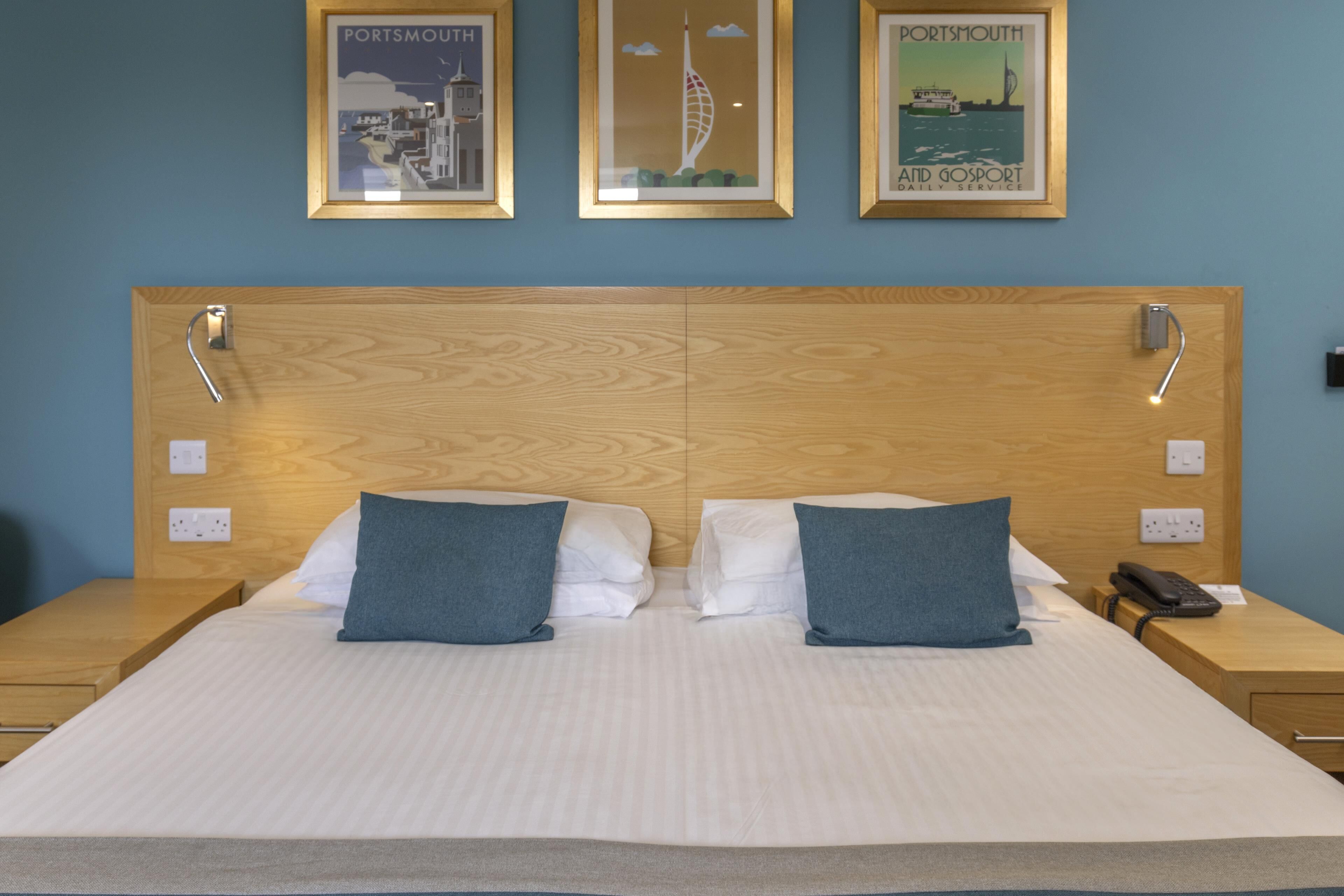 A double bed with two pillows, a wooden headboard, and three framed posters on the wall.