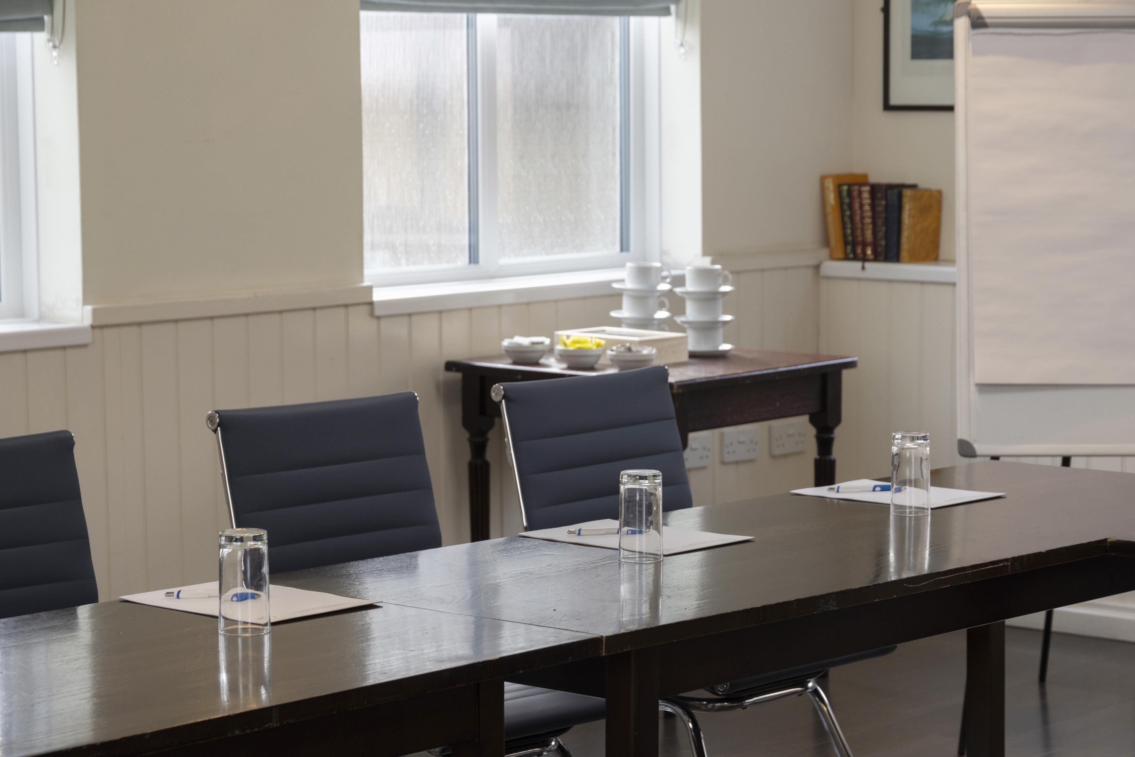 A conference room with a long table, chairs, a whiteboard, and a window with blinds.